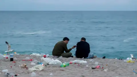 Dos jóvenes conversan al amanecer en la playa de Orzán, en A Coruña, rodeados de basura Dos jóvenes conversan al amanecer en la playa de Orzán, en A Coruña, rodeados de basura