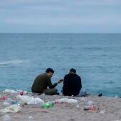 Dos jóvenes conversan al amanecer en la playa de Orzán, en A Coruña, rodeados de basura 