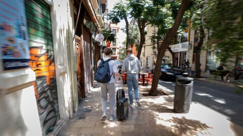 Dos turistas recorren con sus maletas el casco antiguo de la ciudad de València. 