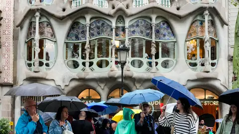 Varios turistas se protegen de la lluvia este lunes en las inmediaciones de la Casa Batlló del paseo de Gracia de Barcelona. Brusco cambio de tiempo este fin de semana: bajada radical de temperaturas y tormentas con granizo en estas zonas
