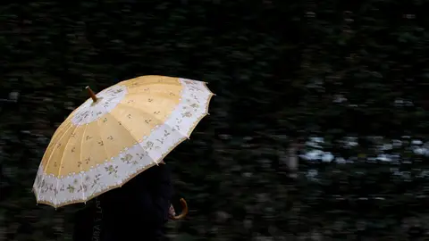 Imagen de archivo de una persona protegiéndose de la lluvia con un paraguas. Las temperaturas se moderan el domingo aunque la inestabilidad y las lluvias se mantienen en varias zonas