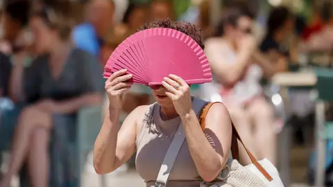 Una mujer se protege con un abanico del sol y del calor . Una mujer se protege con un abanico del sol y del calor .