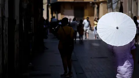 Una mujer se protege del sol y del calor con un parasol La AEMET avisa de la llegada de la primera ola de calor: estas son las zonas más afectadas por las altas temperaturas