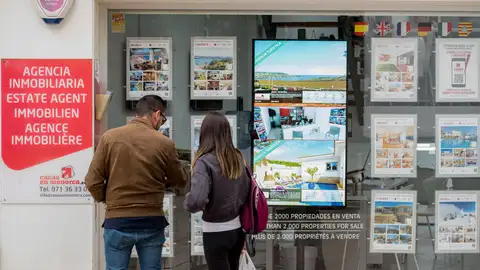 Una pareja observa las propiedades en venta anunciadas en el escaparate de una agencia inmobiliaria. Una pareja observa las propiedades en venta anunciadas en el escaparate de una agencia inmobiliaria.