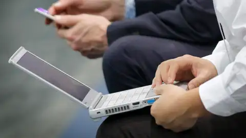 Dos visitantes utilizan un ordenador portatil y un smartphone en una feria tecnológica en una imagen de archivo. Dos visitantes utilizan un ordenador portatil y un smartphone en una feria tecnológica en una imagen de archivo.