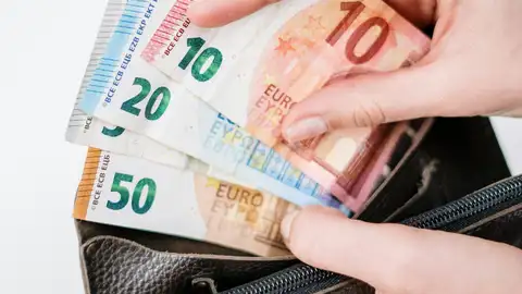 Una mano sosteniendo dinero y un monedero Una mano sosteniendo dinero y un monedero