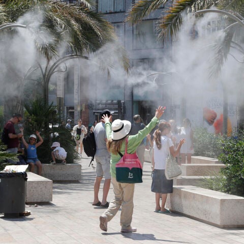 En la imagen, varios turistas tratan de mitigar el calor bajo una nube de agua vaporizada en la plaza de la Reina de Valencia.