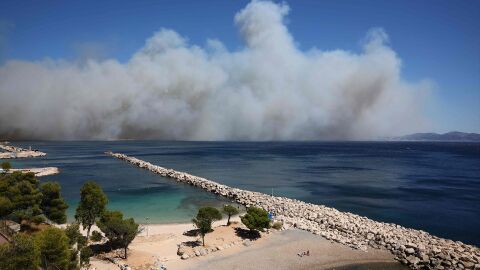 Los ba&ntilde;istas descansan en la Plage des Corbi&egrave;res, en las afueras de Marsella, en el sur de Francia, mientras el humo de un incendio forestal arde en el fondo.