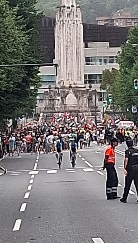 Ciclistas buscando los autocares de sus escuadras y manifestantes al fondo