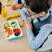 Un niño frente a una táper con frutas y verduras