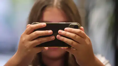 Una chica consulta su teléfono móvil, en una fotografía de archivo. Una chica consulta su teléfono móvil, en una fotografía de archivo.