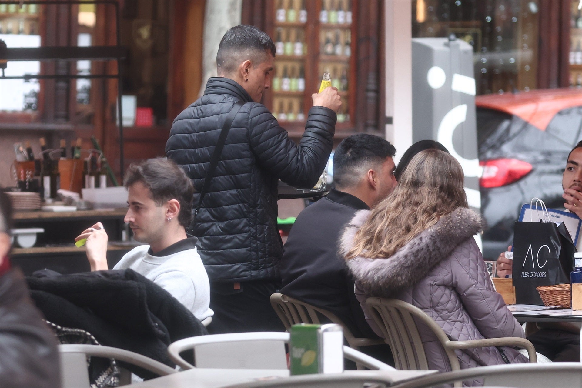 Un camarero atiende a varios clientes en una terraza de un bar. Un camarero atiende a varios clientes en una terraza de un bar.