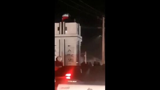 Un hombre se sube encima de un monumento y coloca la bandera pre-revolucionaria