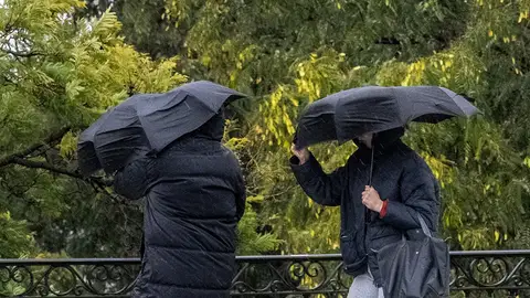 Dos personas se protegen de la lluvia y el viento Vuelve la lluvia: qué comunidades está en alerta y pronóstico de la Aemet para el fin de semana