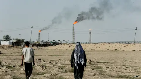 Personas caminan junto a tierras de cultivo cerca del yacimiento petrolífero de Zubair, mientras las llamaradas de gas se elevan a lo lejos, en Zubair Mishrif, Basora, Irak. Personas caminan junto a tierras de cultivo cerca del yacimiento petrolífero de Zubair, mientras las llamaradas de gas se elevan a lo lejos, en Zubair Mishrif, Basora, Irak.