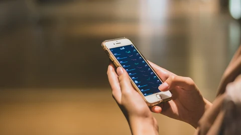 Imagen de archivo de un joven que mira el estado de sus inversiones en su teléfono móvil.