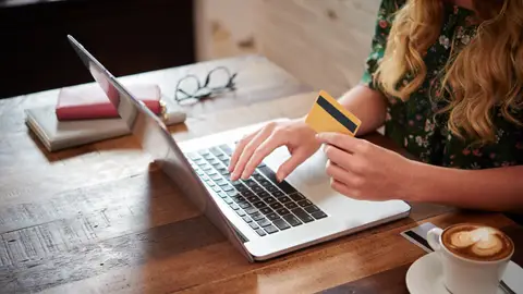 Una mujer sostiene una tarjeta de crédito mientras usa el ordenador Una mujer sostiene una tarjeta de crédito mientras usa el ordenador