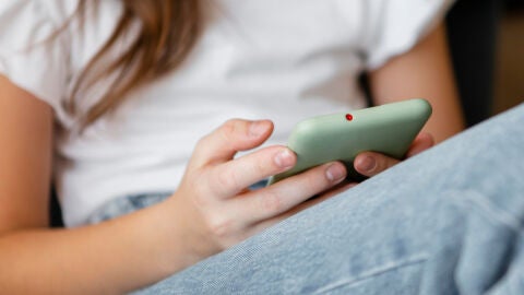 Una adolescente sostiene un tel&eacute;fono m&oacute;vil. 