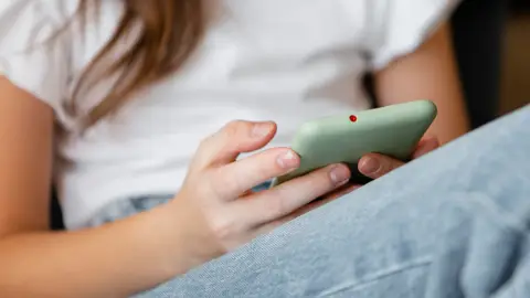 Una adolescente sostiene un teléfono móvil. Una adolescente sostiene un teléfono móvil.