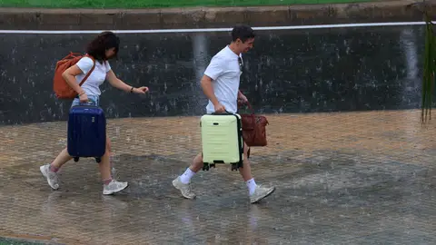 Dos personas con equipaje caminan bajo la lluvia en el aeropuerto de Manises (València). Dos personas con equipaje caminan bajo la lluvia en el aeropuerto de Manises (València).