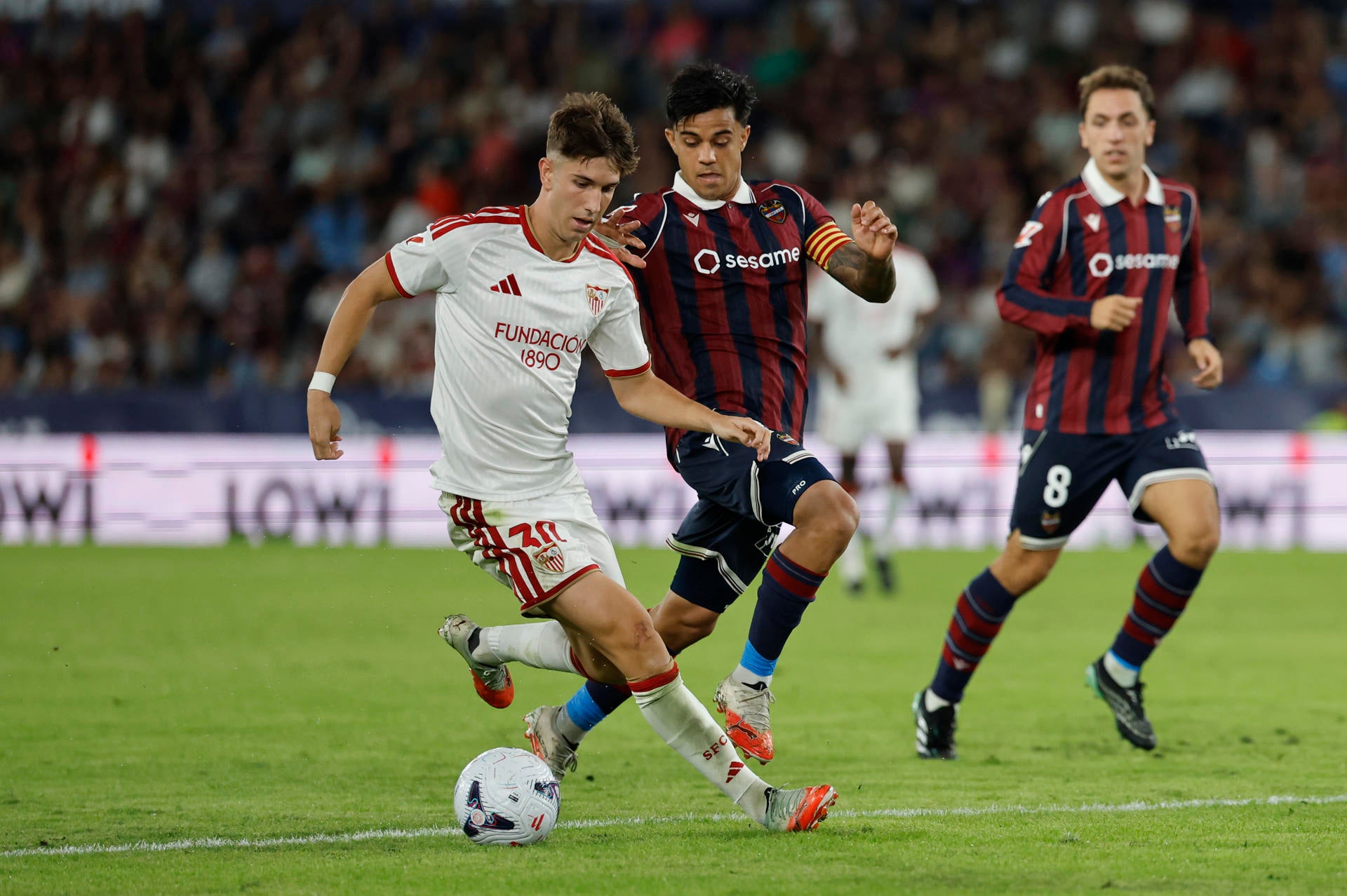 El delantero del Sevilla Miguel Sierra (i) juega un balón ante Roger Brugué (c), del Levante, durante el partido correspondiente a la octava jornada de LaLiga EA Sports que UD Levante y Sevilla FC disputaron en el estadio Ciutat de Valencia. El delantero del Sevilla Miguel Sierra (i) juega un balón ante Roger Brugué (c), del Levante, durante el partido correspondiente a la octava jornada de LaLiga EA Sports que UD Levante y Sevilla FC disputaron en el estadio Ciutat de Valencia.