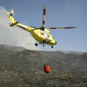 Un helicóptero lleva agua para arrojar sobre el incendio Un helicóptero lleva agua para arrojar sobre el incendio