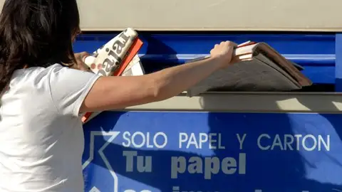 Una persona reciclando papel en el contenedor azul Una persona reciclando papel en el contenedor azul