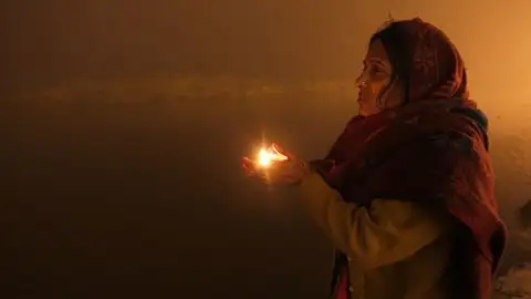 Tradiciones sagradas en la India - Contraparte Una joven india sostiene una vela mientras reza después de tomar un baño sagrado en Sangam durante el festival Magh Mela.