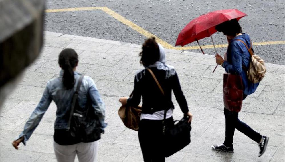 Paseantes tratan de cubrirse de las fuertes lluvias con paraguas