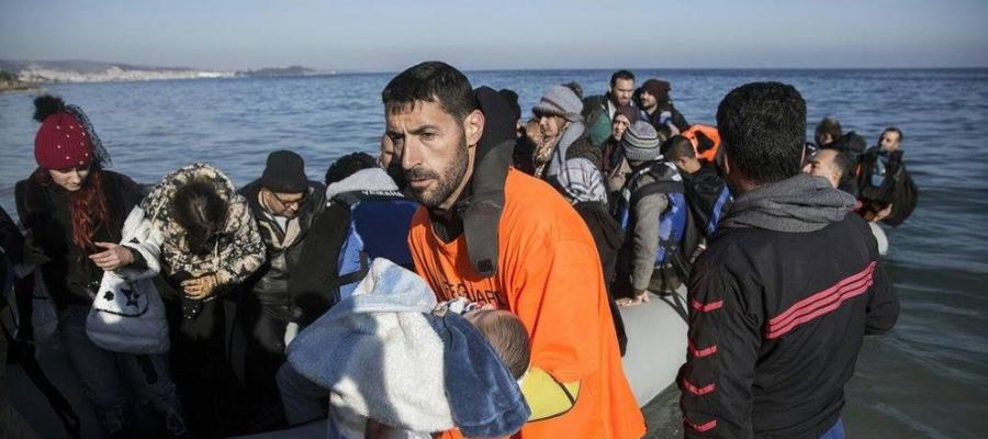 Un miembro de la asociación Proem-Aid desembarca a un bebé de una barca repleta de refugiados en lesbos 