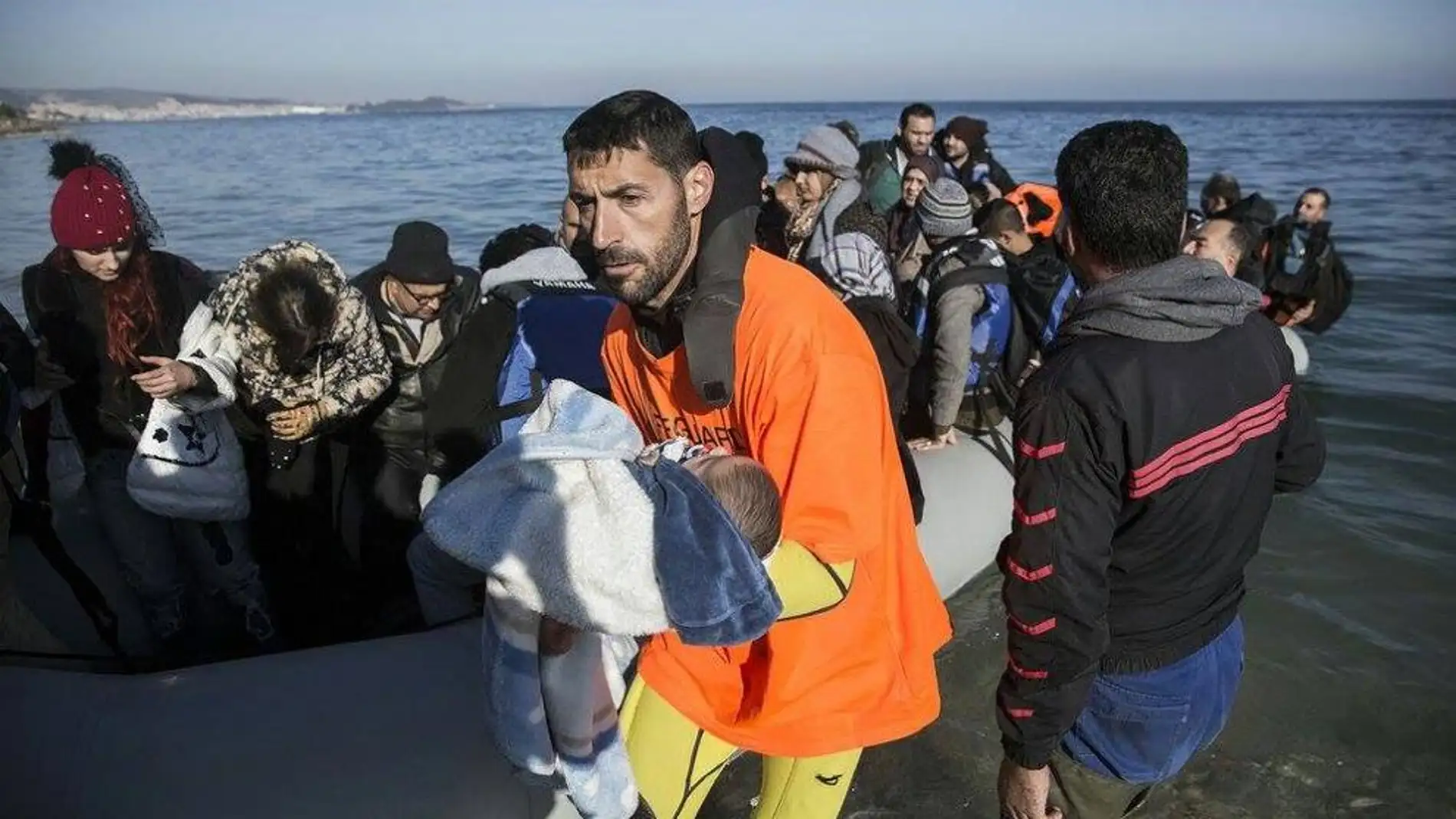 Un miembro de la asociación Proem-Aid desembarca a un bebé de una barca repleta de refugiados en lesbos 