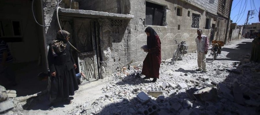 Varias personas inspeccionan edificios en ruinas tras los bombardeos en el pueblo de Deir al Asafi, al sureste de Damasco (Siria)