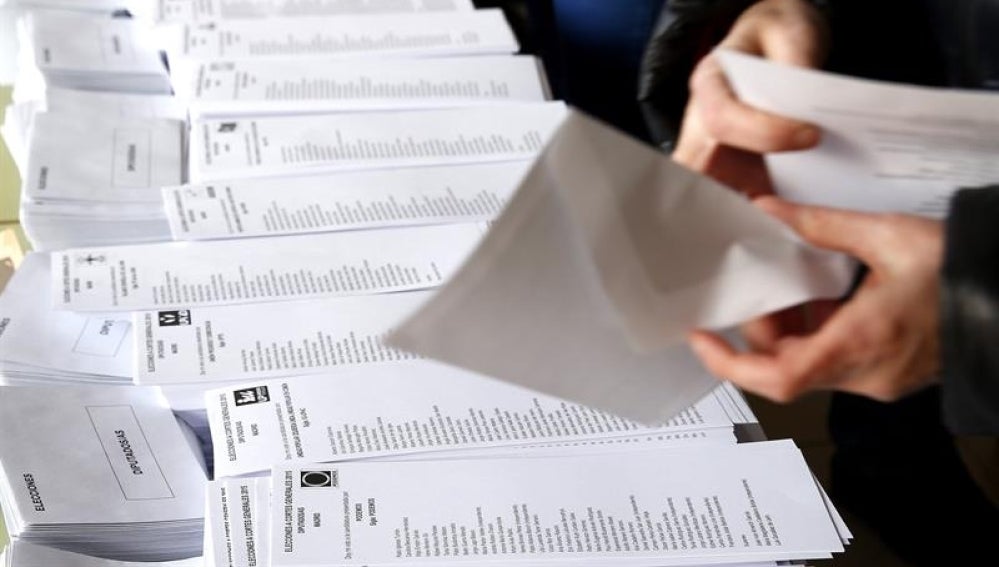  Una persona selecciona una de las papeletas dispuestas en el colegio electoral