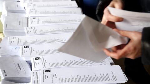  Una persona selecciona una de las papeletas dispuestas en el colegio electoral