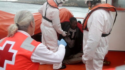 Personal de Cruz Roja ayudan a levantarse a unos inmigrantes que viajaban en una patera y que fueron rescatados por Salvamento Mar&iacute;timo