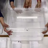 Varias manos sujetando una urna sobre las papeletas de unas elecciones Varias manos sujetando una urna sobre las papeletas de unas elecciones