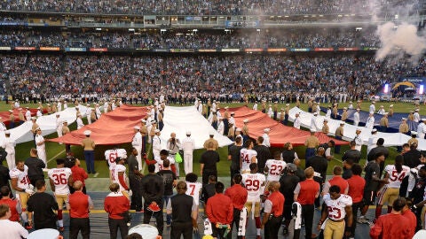 Colin Kaepernick, en la parte inferior de la fotograf&iacute;a (lleva el dorsal 7), de rodillas mientras suena el himno de Estados Unidos