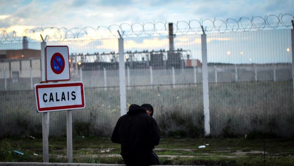 Un joven permanece sentado frente a una verja en del campamento de inmigrantes situado en Calais