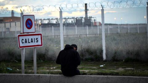 Un joven permanece sentado frente a una verja en del campamento de inmigrantes situado en Calais