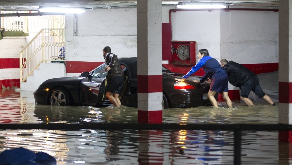 Varias personas intentan sacar el coche de un garaje inundado