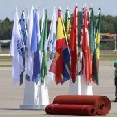 Unos operarios esperan junto a banderas y alfombras rojas preparadas en el aeropuerto para la llegada de los líderes