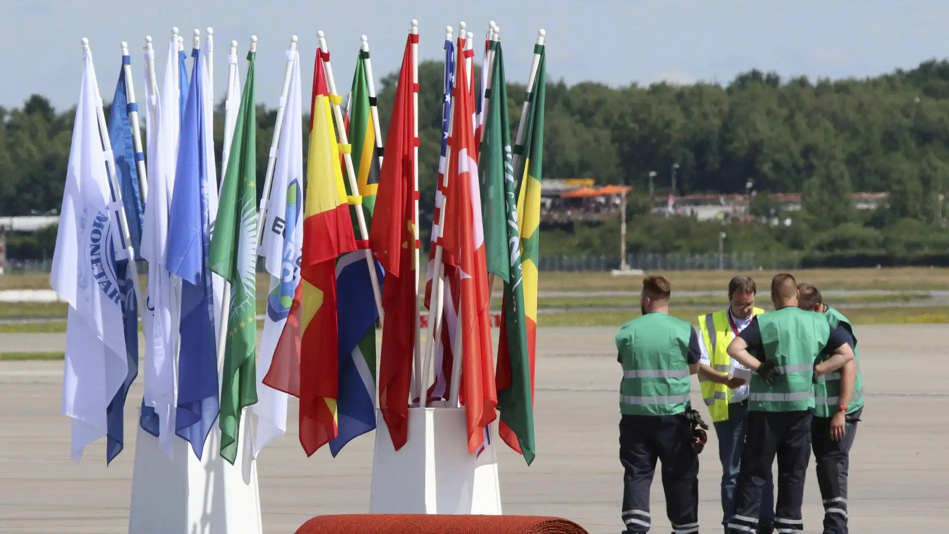 Unos operarios esperan junto a banderas y alfombras rojas preparadas en el aeropuerto para la llegada de los líderes
