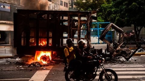 Dos personas pasan por delante de un cami&oacute;n calcinado en Venezuela