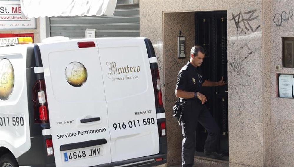 Un agente de la Policía Nacional junto a una furgoneta de los servicios funerarios en el domicilio de la mujer fallecida en Alcorcón