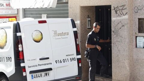 Un agente de la Polic&iacute;a Nacional junto a una furgoneta de los servicios funerarios en el domicilio de la mujer fallecida en Alcorc&oacute;n