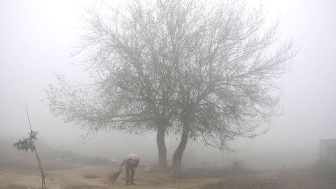 Un hombre indio barre el suelo con neblina y niebla a primera hora de la ma&ntilde;ana en las afueras de Amritsar, India
