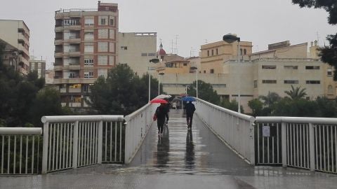 Personas con paraguas en la Pasarela del Mercado de Elche.