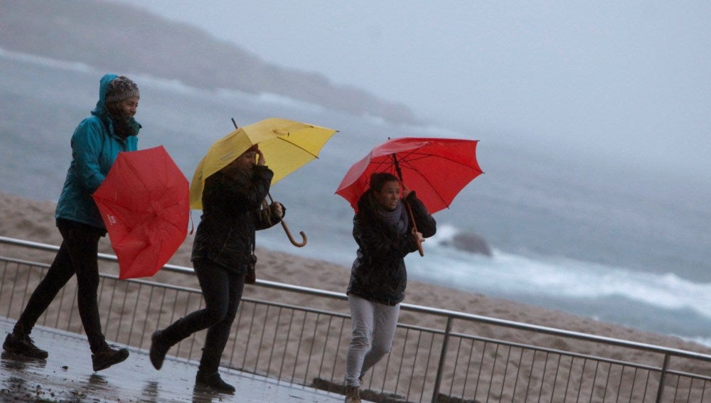 Tres mujeres se protegen de la lluvia en el paseo marítimo de A Coruña