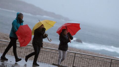Tres mujeres se protegen de la lluvia en el paseo mar&iacute;timo de A Coru&ntilde;a
