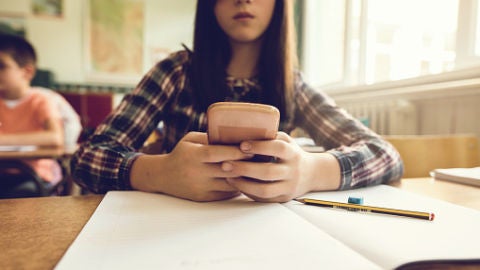 Una adolescente mira su m&oacute;vil en clase